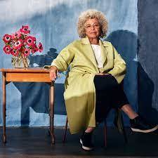Angela Davis sitting next to a table with flowers on it, and a blue backdrop