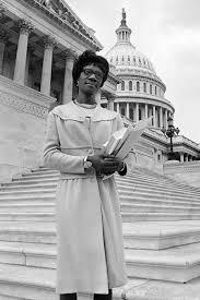 Shirley Chisholm standing in front of a government building holding papers