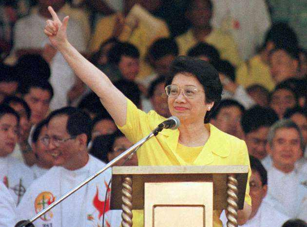 Corazon Aquino at a rally in a yellow shirt and people in a crowd behind her